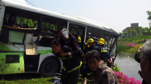 公交車被撞到幾十米外的河邊，車體前部受損嚴(yán)重。圖為接警后，消防人員很快來到現(xiàn)場，將乘客從車廂里逐個(gè)救出。