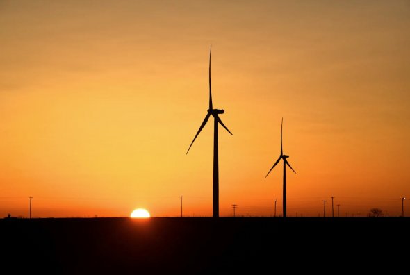 2019年2月12日，美國德克薩斯州大斯普林的二疊紀盆地石油和天然氣生產區，風力渦輪機在日出時運行。